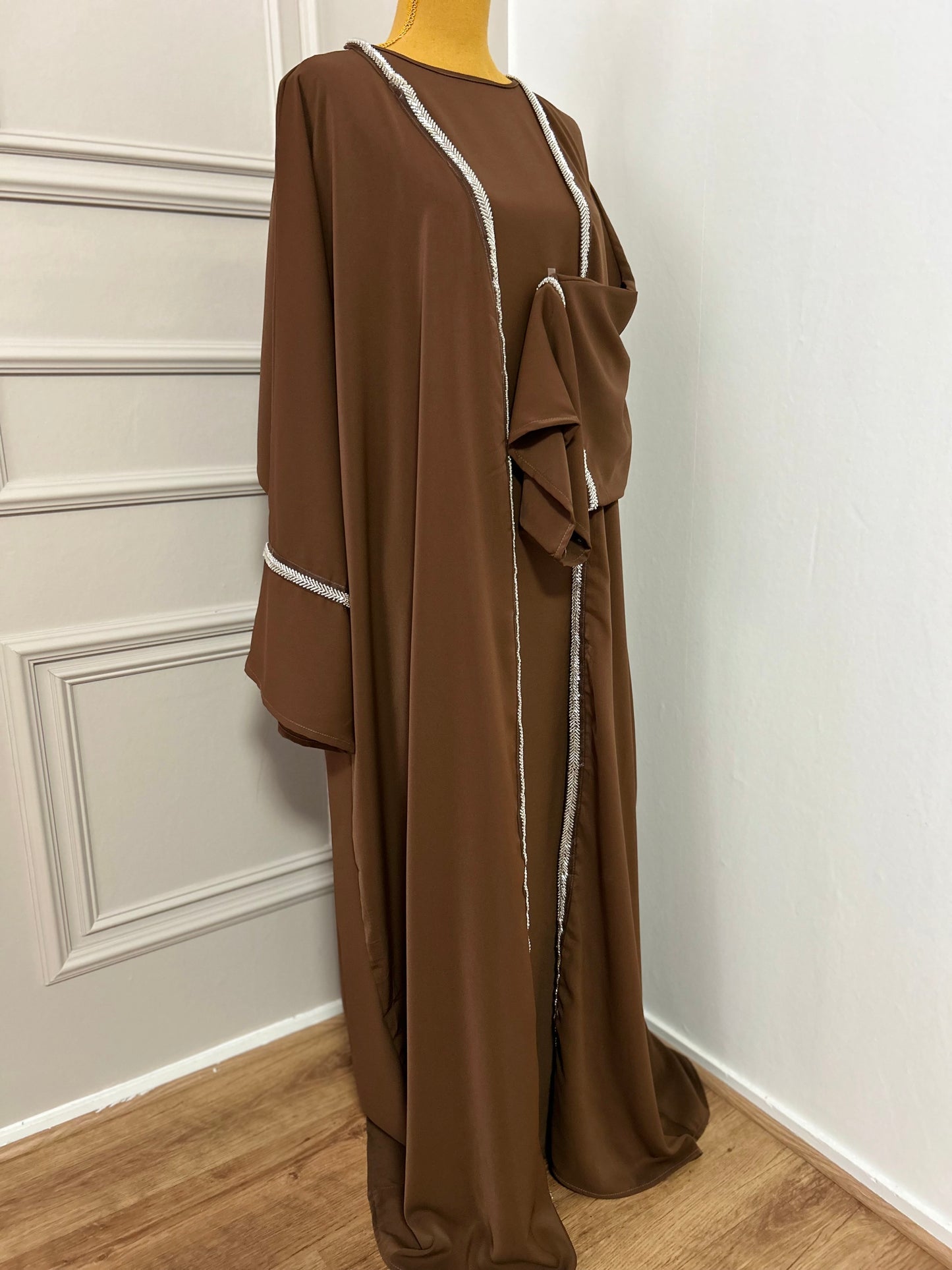 Craquez pour cette abaya marron 2 pièces alliant confort et élégance, avec son kimono orné de strass et sa sous-robe fluide. Idéale pour les occasions ou un style raffiné au quotidien.