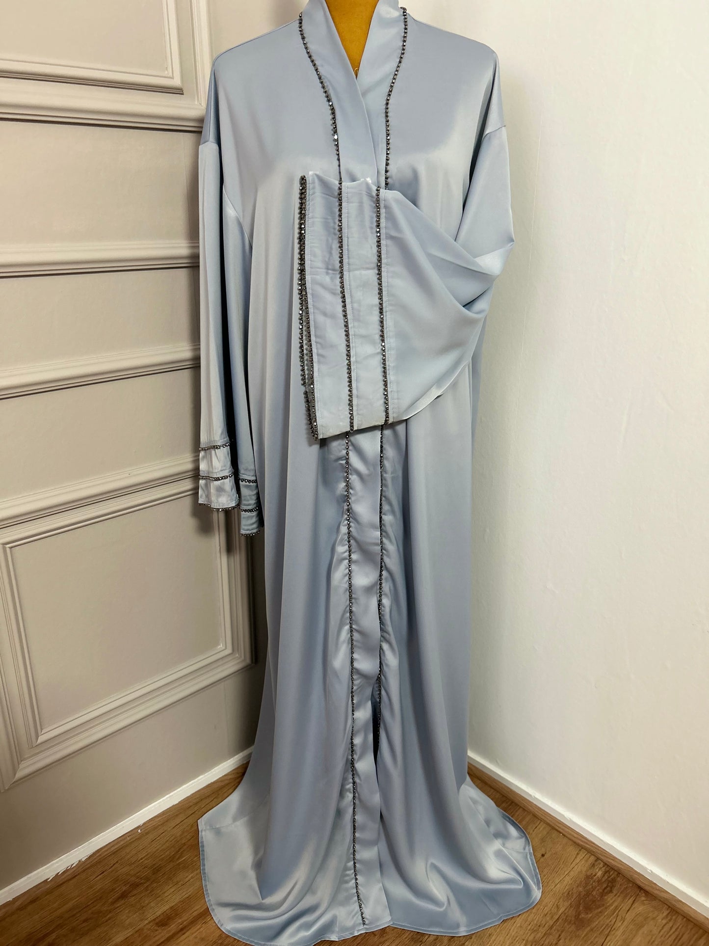 Abaya satinée bleu ciel avec finitions en perles noires, coupe ample et élégante.
