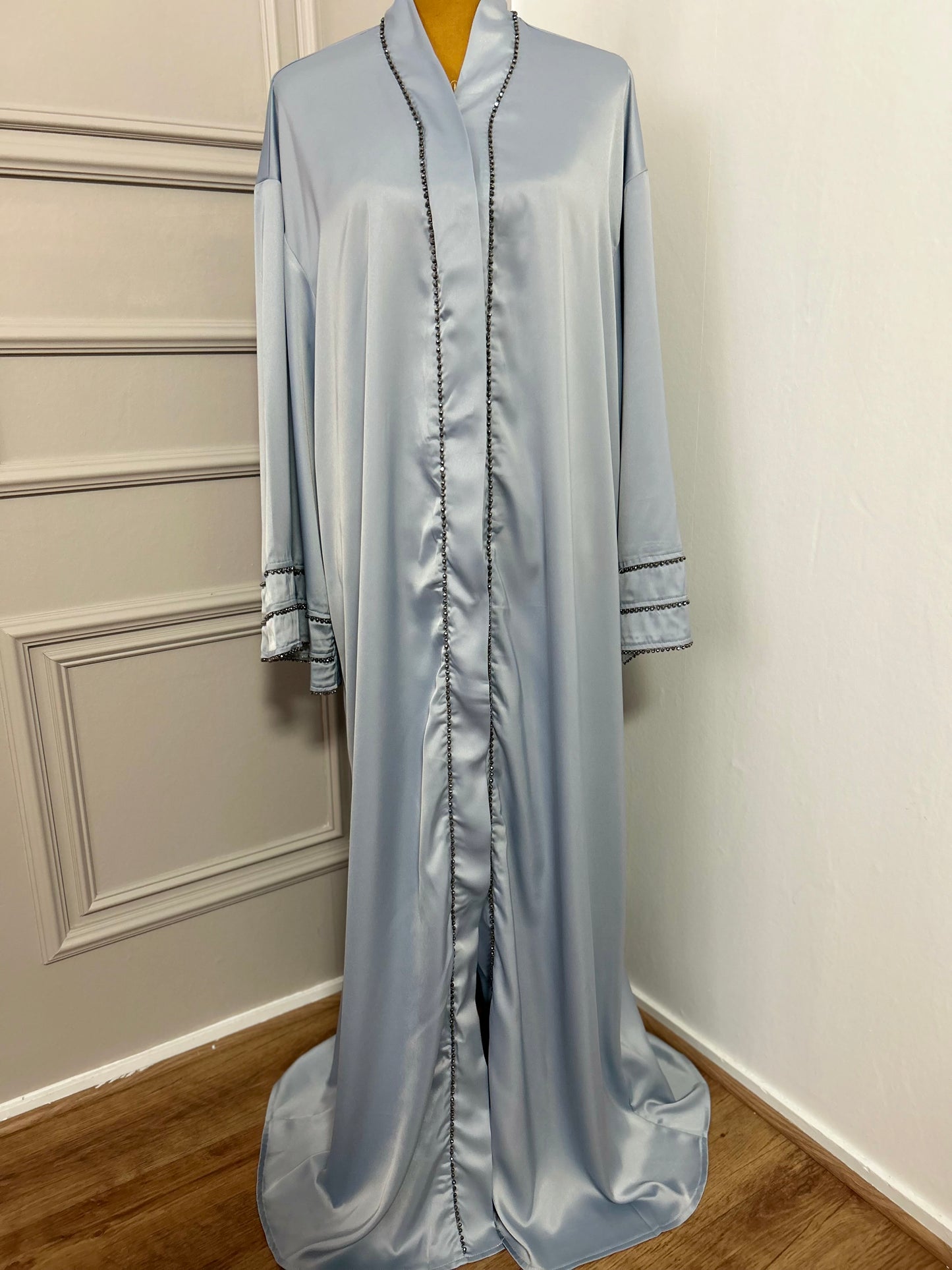 Abaya satinée bleu ciel avec finitions en perles noires, coupe ample et élégante.