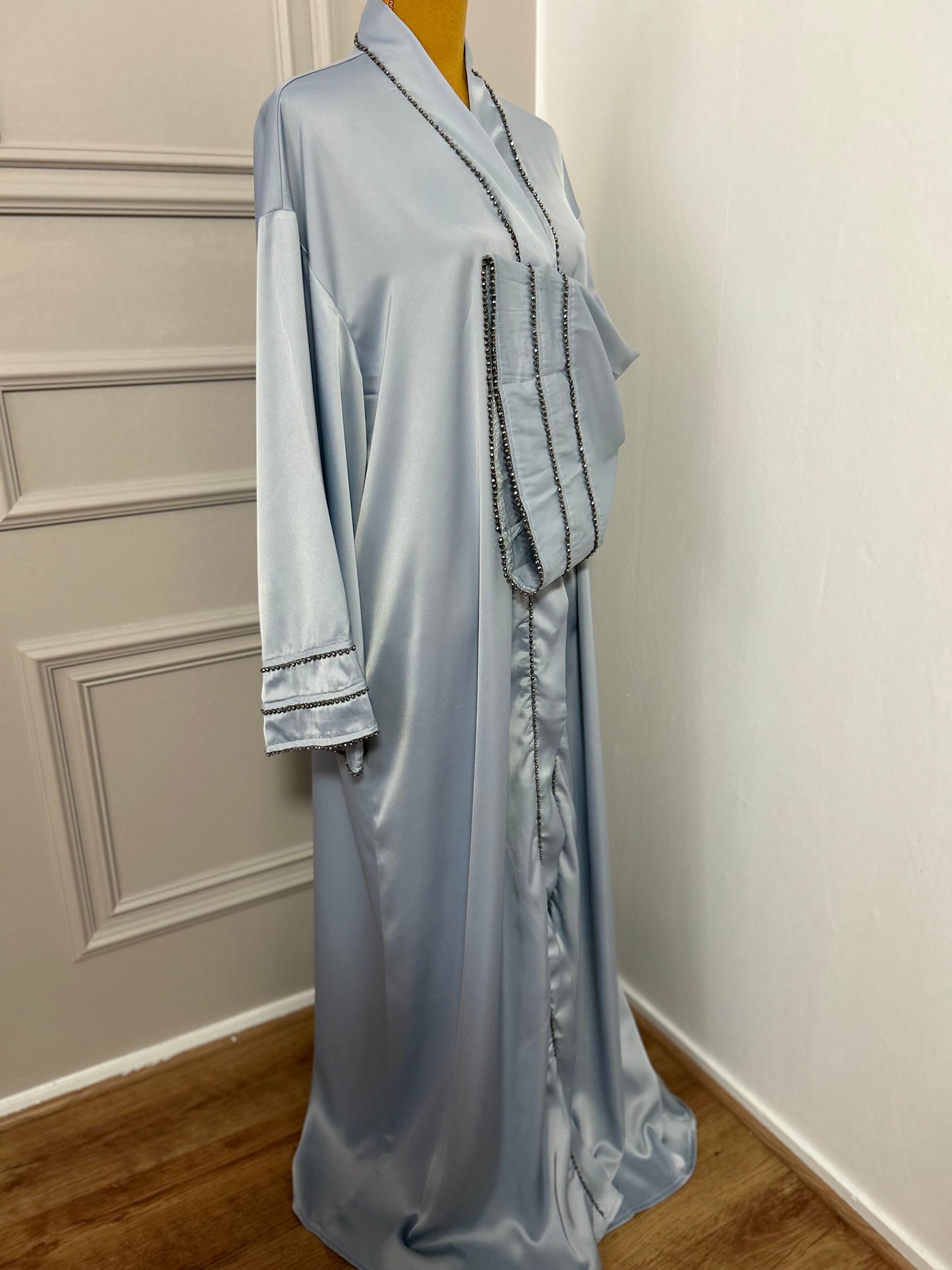 Abaya satinée bleu ciel avec finitions en perles noires, coupe ample et élégante.