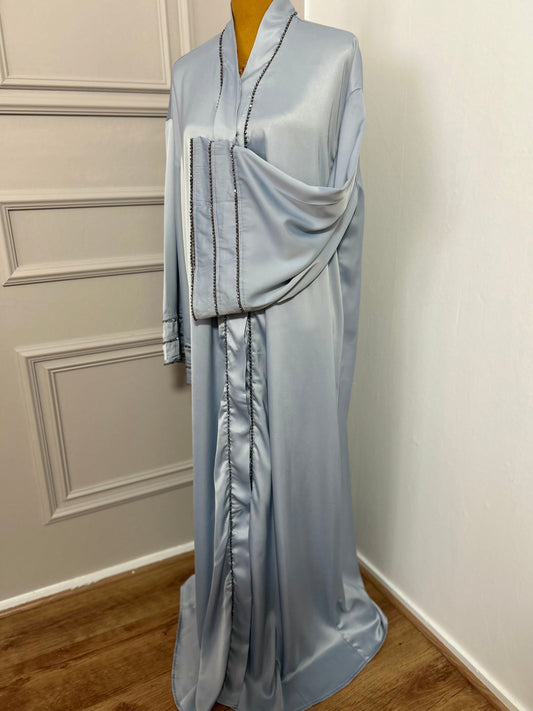 Abaya satinée bleu ciel avec finitions en perles noires, coupe ample et élégante.