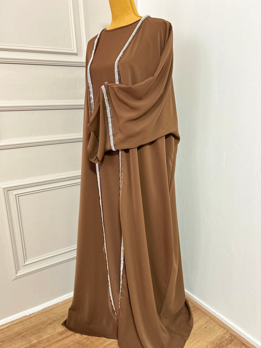 Craquez pour cette abaya marron 2 pièces alliant confort et élégance, avec son kimono orné de strass et sa sous-robe fluide. Idéale pour les occasions ou un style raffiné au quotidien.
