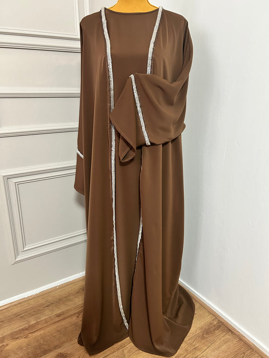 Craquez pour cette abaya marron 2 pièces alliant confort et élégance, avec son kimono orné de strass et sa sous-robe fluide. Idéale pour les occasions ou un style raffiné au quotidien.