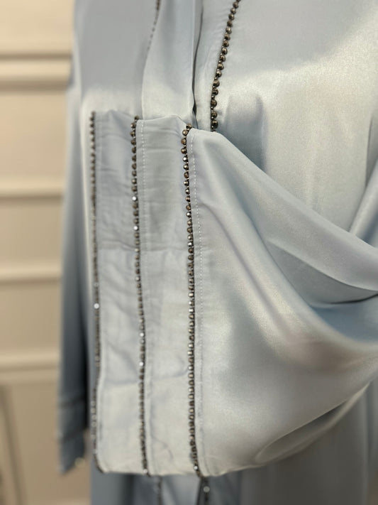 Abaya satinée bleu ciel avec finitions en perles noires, coupe ample et élégante.
